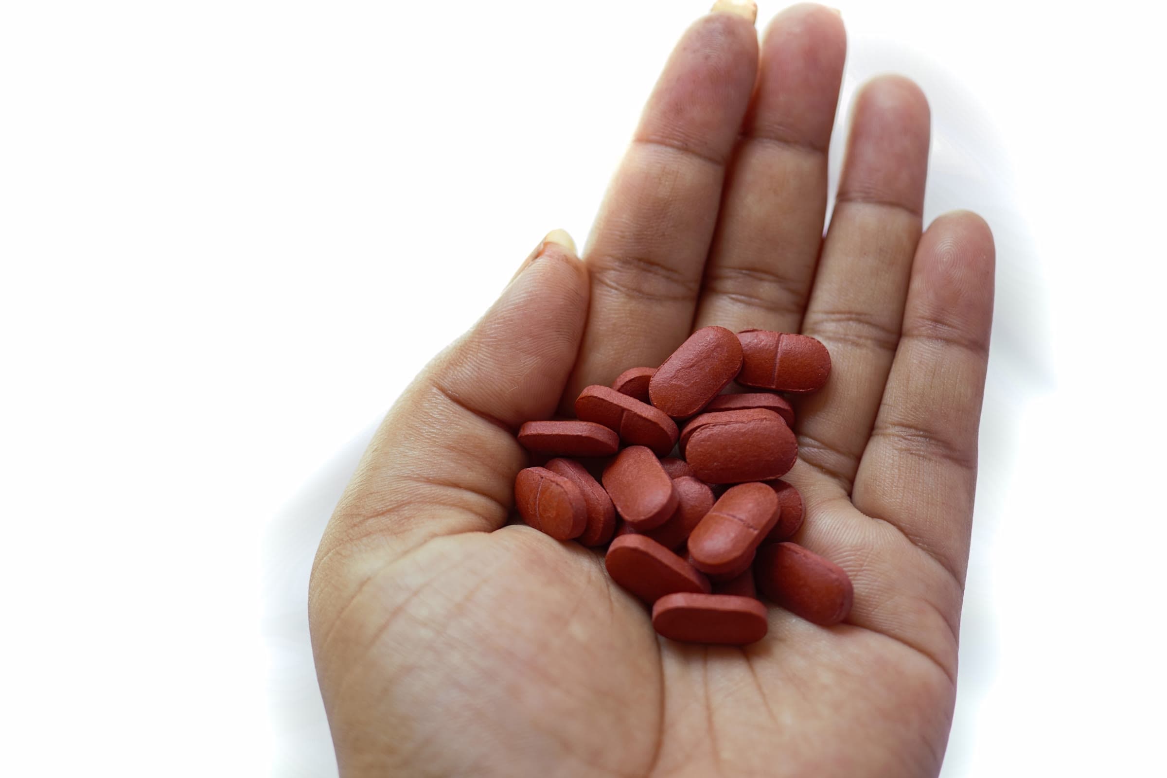An open palm holding a small pile of reddish-brown iron supplement tablets.